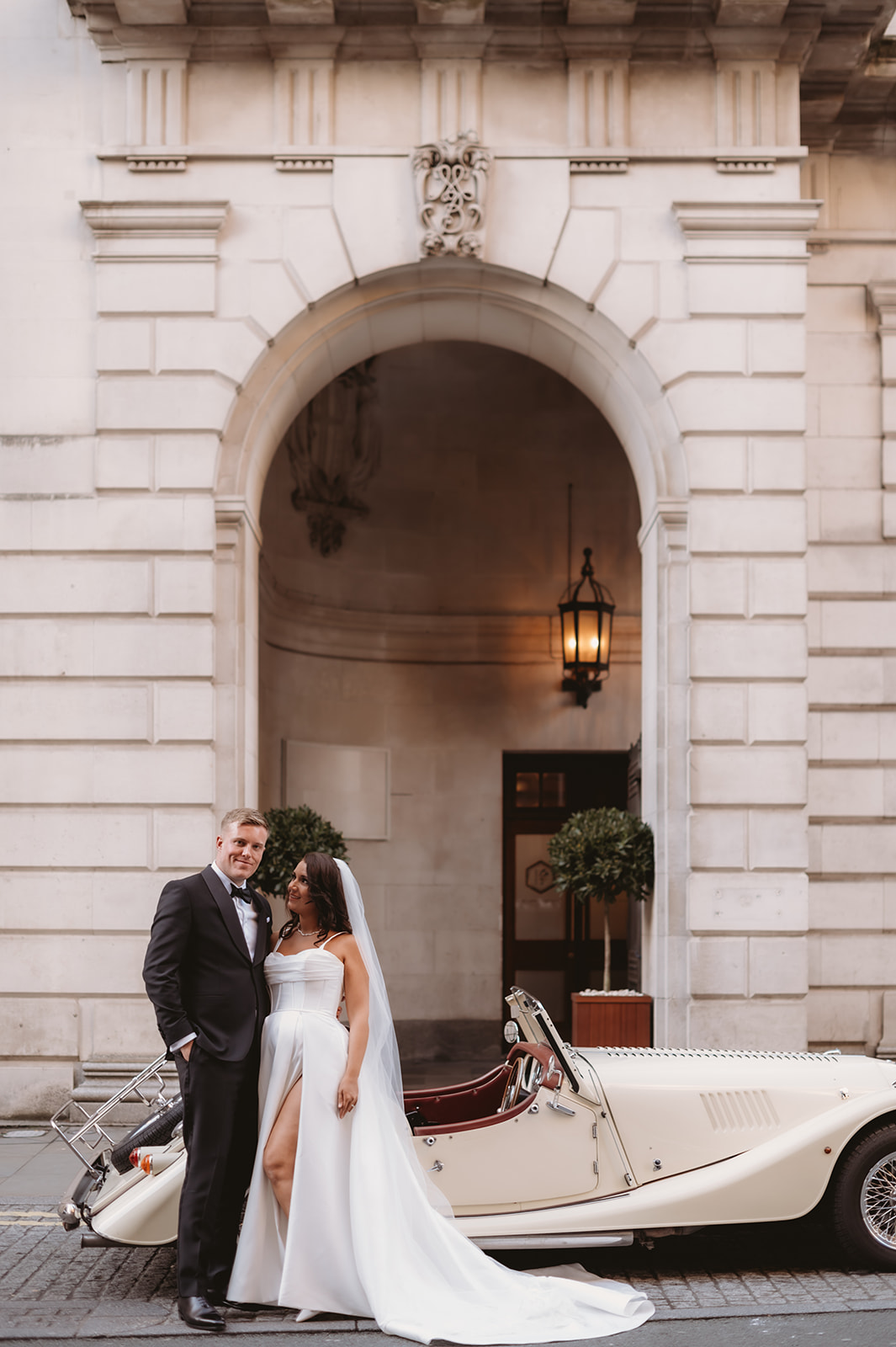 Zoe and Dan beside the ivory Morgan outside their wedding venue